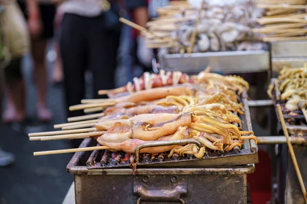 Grilled squid on a cast iron grill over a charcoal grill, Calamari fish bbq on the market, China town Bangkok Thailand, colorful streets of China Town Bangkok.