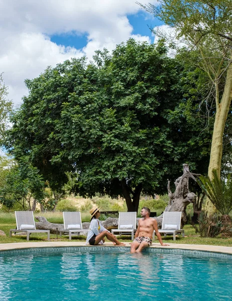 couple men and women on safari in South Africa relaxing by the pool of a luxury safari lodge , Asian women and European men on safari in South Africa