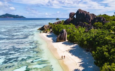 Anse Source dArgent, La Digue Seychelles, Anse Source DArgent, La Digue Seychelles 'de lüks bir tatil sırasında tropikal bir plajda yaşayan birkaç beyaz erkek ve Asyalı kadın.