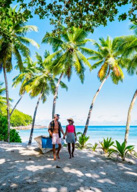 Mahe Seyşeller, palmiye ağaçları ve Mahe Seyşeller 'de mavi bir okyanusu olan tropikal bir plaj. Anse Takamaka plajı Mahe Seyşeller. Tatilde olan çift erkek ve kadın Seyşeller
