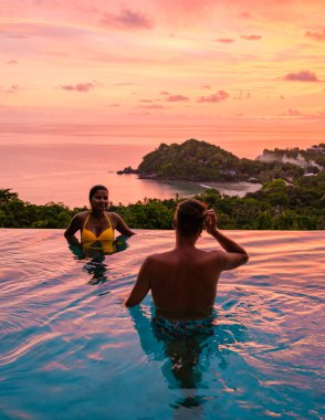 Genç bir çift, tropik bir adada tatil yaparken yüzme havuzunda. Erkek ve kadın gün batımında sonsuz havuzda. Tayland 'da lüks bir havuz villasında lüks bir tatil.