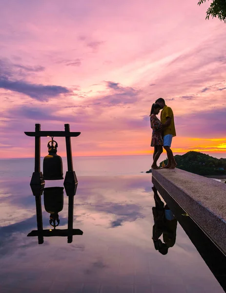 a young couple of men and women at a swimming pool during a vacation on a tropical island. man and woman in infinity pool during sunset. luxury vacation in Thailand pool of a luxury pool villa