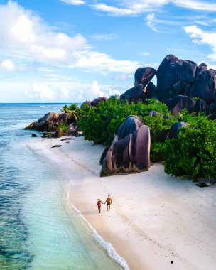 Anse Source dArgent plajı, La Digue Adası, Seyshelles, La Digue Seyşeller 'in insansız hava görüntüsü tropik adanın kuş bakışı görüntüsü, günbatımında sahilde yürüyen iki erkek ve kadın.