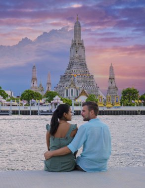 Wat Arun tapınağı Bangkok Tayland, Şafak Tapınağı, Budist tapınağı Chao Phraya Nehri 'nin yanında. Güzel Wat Arun akşam üstü, çift Asyalı kadın ve Avrupalı erkek gün batımını izliyor.