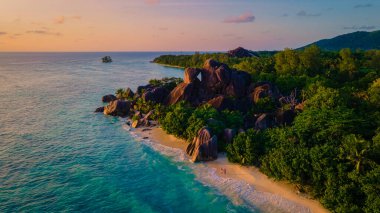 Anse Source dArgent plajı, La Digue Adası, Seyshelles, La Digue Seyşeller 'in insansız hava görüntüsü tropik adanın kuş bakışı görüntüsü, günbatımında sahilde yürüyen iki erkek ve kadın.