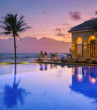 Genç bir çift, tropik bir adada tatil yaparken yüzme havuzunda. Erkek ve kadın gün batımında sonsuz havuzda. Tayland 'da lüks bir havuz villasında lüks bir tatil.