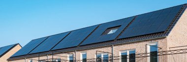Newly build houses with solar panels attached on the roof against a sunny sky Close up of a new building with black solar panels. Zonnepanelen, Zonne energie, Translation: Solar panel, , Sun Energy. 