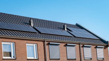 Newly build houses with solar panels attached on the roof against a sunny sky Close up of a new building with black solar panels. Zonnepanelen, Zonne energie, Translation: Solar panel, , Sun Energy. 