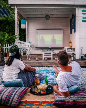 couple looking at movies in the garden at night, people looking for movies in the garden, garden cinema at night at home. 