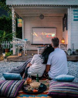 couple looking at movies in the garden at night, people looking for movies in the garden, garden cinema at night at home. 