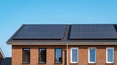 Newly build houses with solar panels attached on the roof against a sunny sky Close up of a new building with black solar panels. Zonnepanelen, Zonne energie, Translation: Solar panel, , Sun Energy. 