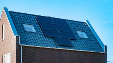 Newly build houses with solar panels attached on the roof against a sunny sky Close up of a new building with black solar panels. Zonnepanelen, Zonne energie, Translation: Solar panel, , Sun Energy. 