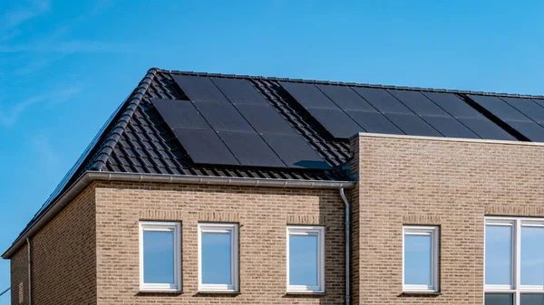 Newly build houses with solar panels attached on the roof against a sunny sky Close up of a new building with black solar panels. Zonnepanelen, Zonne energie, Translation: Solar panel, , Sun Energy. 
