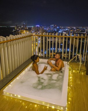 a couple of men and women having a bath on the balcony looking out over the bay of Pattaya, a Thai girl, and a European man on the balcony of an apartment condo in Thailand. 