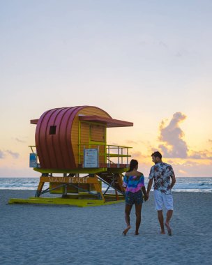 Miami Beach, a couple on the beach at Miami Florida, lifeguard hut Miami Asian women and caucasian men on the beach during sunset