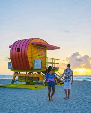 Miami Beach, a couple of men and women on the beach in Miami Florida, lifeguard hut Miami Asian women and caucasian men on the beach during sunset. man and woman relaxing at a lifeguard