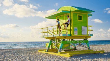 Miami Beach, a couple of men and women on the beach in Miami Florida, lifeguard hut Miami Asian women and caucasian men on the beach during sunset. man and woman relaxing at a lifeguard