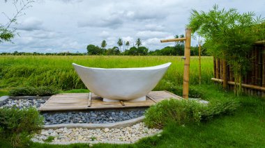 white bathtub outside looking out over a green rice field, bath tub outside on vacation at a homestay in Thailand with a green rice paddy field