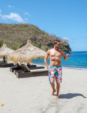 young men in swim short walking on a tropical beach in St Lucia,white beach with palm trees in Saint Lucia Caribbean. The beautiful White sandy beach of Caribbean Gros, umbrellas with chairs