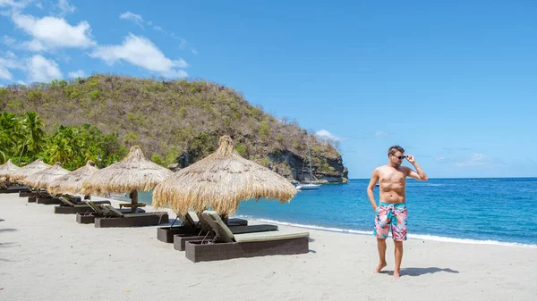 young men in swim short walking on a tropical beach in St Lucia,white beach with palm trees in Saint Lucia Caribbean. The beautiful White sandy beach of Caribbean Gros, umbrellas with chairs