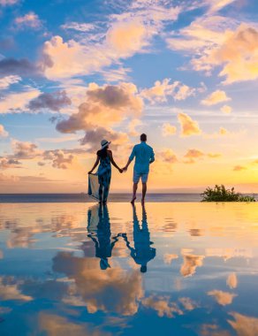 Young men and women watching the sunset with reflection in the infinity swimming pool at Saint Lucia Caribbean, couple at infinity pool during sunset
