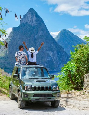 a couple of men and women exploring the Island of St Lucia in a rental car. Mountains of Saint Lucia with in the background the huge pitons in the ocean with palm trees