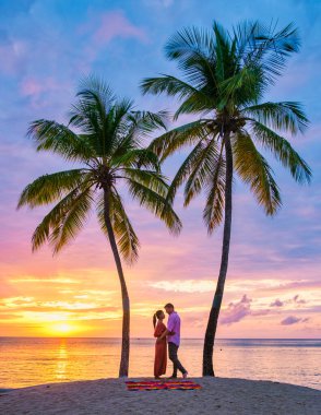 couple on the beach with palm trees watching the sunset at the tropical beach of Saint Lucia or St Lucia Caribbean. men and women on vacation in St Lucia a tropical island with palm trees