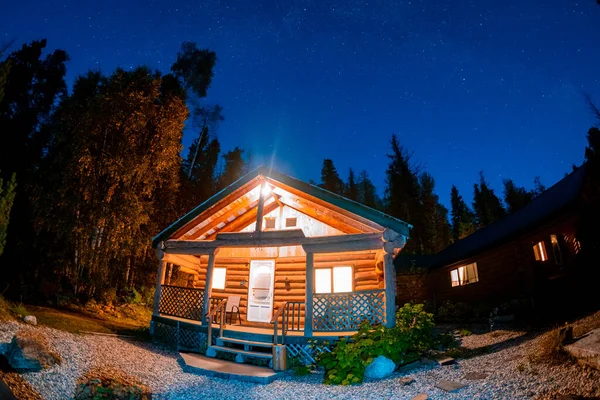 wooden cottage in the woods with starry milky way at night in the sky, night sky with stars. wooden hut camping in the woods