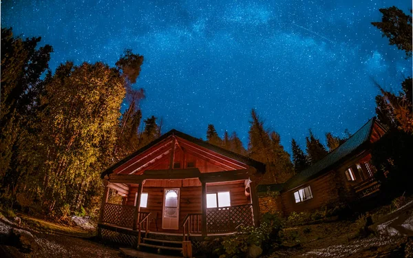 wooden cottage in the woods with starry milky way at night in the sky, night sky with stars. wooden hut camping in the woods