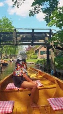 Giethoorn canals Holland, an Asian woman with hat in a wooden boat at the canals of Giethoorn Netherlands. Giethoorn, Netherlands: Giethoorn village with canals and rustic thatched roof houses
