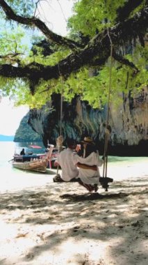 Koh Hong Island Krabi Thailand, a couple of men and women are in a swing on a tropical beach in Thailand. Asian women and Caucasian men on vacation in Thailand