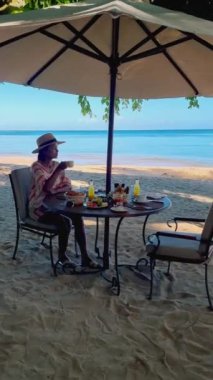 Women having breakfast on the beach in Thailand, a Luxury breakfast table with food and beautiful tropical sea view background, luxury travel, and lifestyle. 