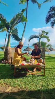Breakfast on the beach in Mauritius, a couple of men and women having a Luxury breakfast table with food and beautiful tropical sea view background, luxury travel, and lifestyle. 