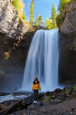 Beautiful waterfall in Canada, couple visit Helmcken Falls, the most famous waterfall in Wells Gray Provincial Park in British Columbia, Canada. Asian woman with a yellow sweater and hat looking at a