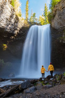 Beautiful waterfall in Canada, couple visit Helmcken Falls, the most famous waterfall in Wells Gray Provincial Park in British Columbia, Canada. couple of men and women standing by a waterfall