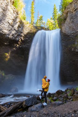 Beautiful waterfall in Canada, couple visit Helmcken Falls, the most famous waterfall in Wells Gray Provincial Park in British Columbia, Canada. couple of men and women standing by a waterfall