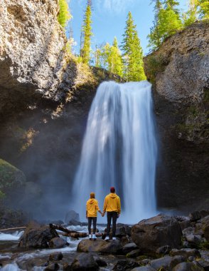 Moul Falls Canada is a Beautiful waterfall in Canada, couple of visits to Moul Falls, the most famous waterfall in Wells Gray Provincial Park. a couple of men and women standing by a waterfall