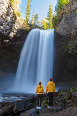 Moul Falls Canada is a Beautiful waterfall in Canada, couple of visits to Moul Falls, the most famous waterfall in Wells Gray Provincial Park. a couple of men and women standing by a waterfall