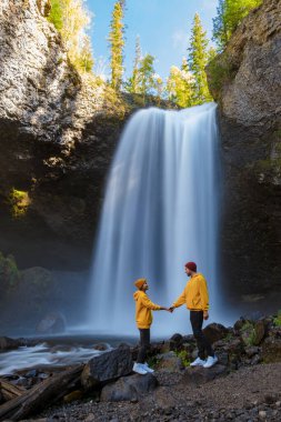 Moul Falls Canada is a Beautiful waterfall in Canada, couple of visits to Moul Falls, the most famous waterfall in Wells Gray Provincial Park. a couple of men and women standing by a waterfall