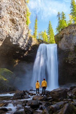 Moul Falls Canada is a Beautiful waterfall in Canada, couple of visits to Moul Falls, the most famous waterfall in Wells Gray Provincial Park. a couple of men and women standing by a waterfall