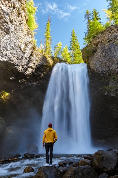 Moul waterfall in Canada, couple visit Moul Falls, the most famous waterfall in Wells Gray Provincial Park in British Columbia, Canada. young men standing looking at a waterfall