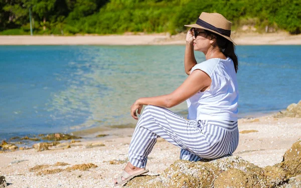young Asian women on the beach sitting on a rock looking over the ocean of Ban Amphur Beach Pattaya Thailand, a beach with beautiful palm trees and a blue ocean in Pattaya Thailand