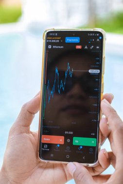 Asian woman checking cryptocurrency on their phone when on holiday , close up of hand and phone with crypto Ethereum currency