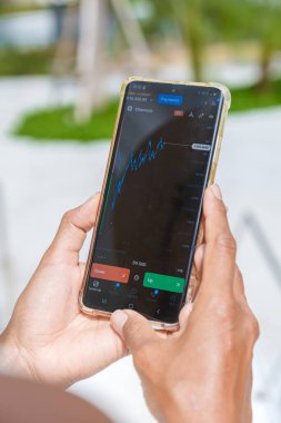 Asian woman checking cryptocurrency on their phone when on holiday , close up of hand and phone with crypto Ethereum currency