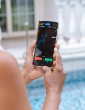 Asian women with hat check Ethereum crypto currency on their phones when on holiday. Asian women trading bitcoin on her phone