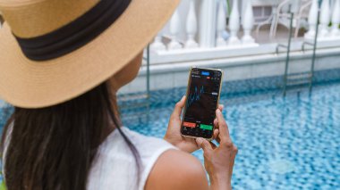 Asian women with hat check Ethereum crypto currency on their phones when on holiday. Asian women trading bitcoin on her phone
