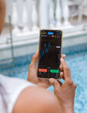 Asian women with hat check Ethereum crypto currency on their phones when on holiday. Asian women trading bitcoin on her phone