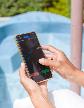 Asian women with hat check Ethereum crypto currency on their phones when on holiday. Asian women trading bitcoin on her phone