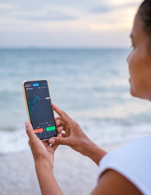 Asian women checking cryptocurrency on their phones when on holiday, women checking their phone on vacation in Thailand