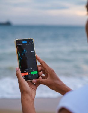 Asian women checking cryptocurrency on their phones when on holiday, women checking their phone on vacation in Thailand